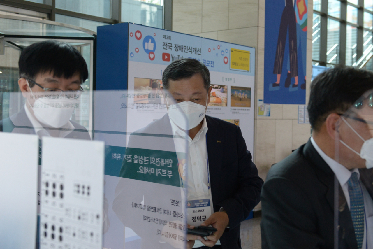 정덕균 포스코ICT 사장이 장애인식개선 유튜브 공모전 전시 중 점자명함 제작을 체험하고 있다. [포스코ICT 제공]