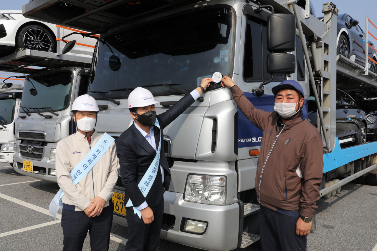 (왼쪽부터) 현대글로비스 국내물류사업부 김보성 상무, 한국교통안전공단 검사전략실 오태석 실장, 현대글로비스 위수탁 차주 박국만 기사가 4일 현대글로비스 충주사무소에서 ‘카캐리어 안전운행 캠페인’의 일환으로 작업자 추락방지 안전난간대를 설치한 자동차운반트럭에 인증 스티커를 부착하고 있다. [현대글로비스 제공]