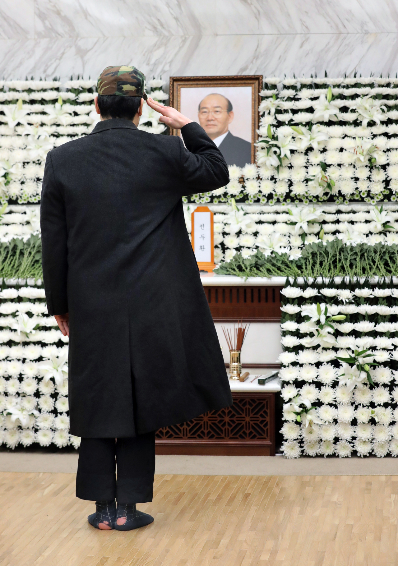 지난 24일 서울 서대문구 신촌 세브란스병원 장례식장에 마련된 전두환 전 대통령 빈소를 찾은 한 조문객이 전투모를 꺼내쓰고 경례를 하고 있다. [공동취재]