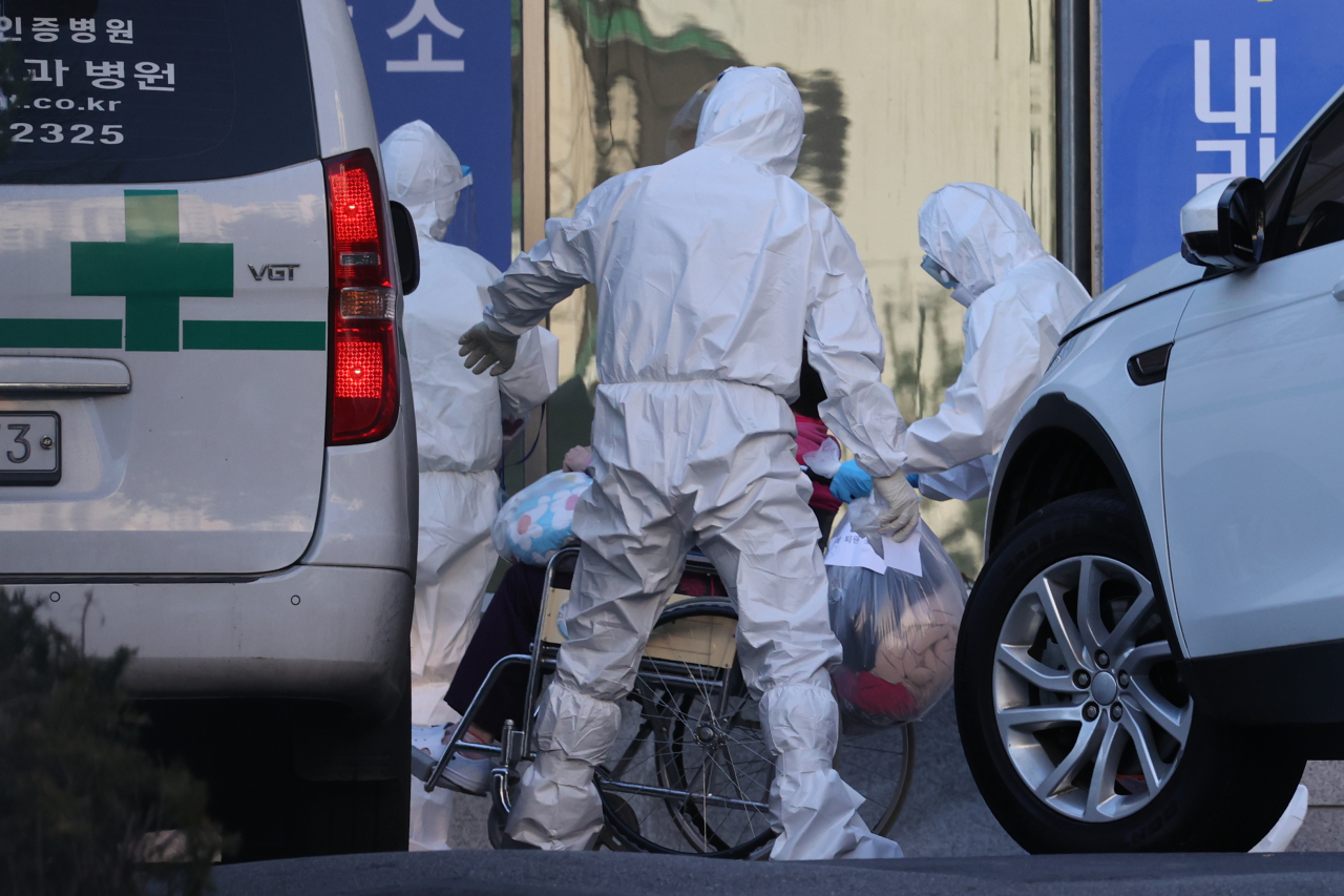 This photo taken Monday outside a hospital in Eunpyeong, Seoul's northern district, shows health care workers assisting a COVID-19 patient in wheelchair. (Yonhap)