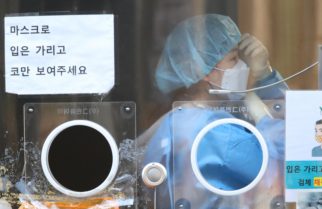 21일 오전 서울역 광장에 마련된 코로나19 임시선별검사소에서 한 의료진이 검체 검사 전 방호복 차림을 점검하고 있다. [연합]