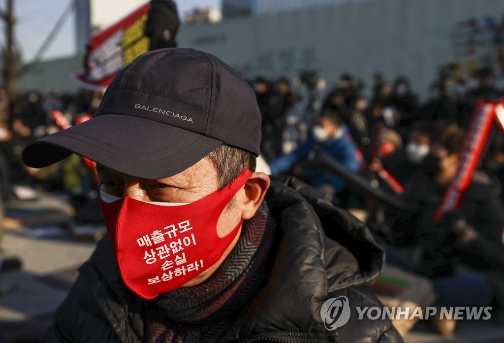 22일 오후 서울 광화문시민열린마당에서 열린 '코로나19 대응 전국자영업자비상대책위원회(자영업비대위) 정부 방역 대책 반대 총궐기 대회'에서 참석자가 관련 내용이 적힌 마스크를 쓴 채 사회자의 발언을 듣고 있다. [연합]