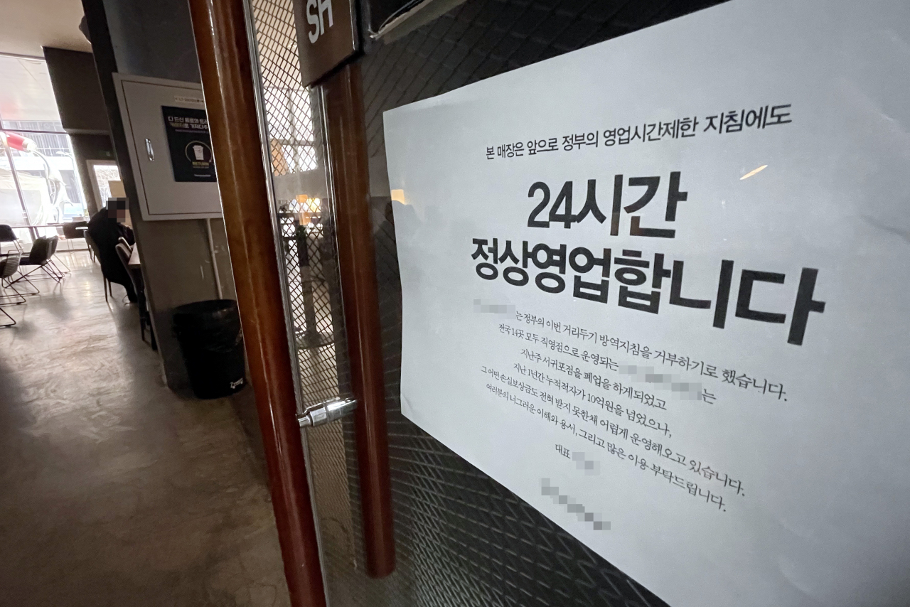 코로나19 확산으로 전국에 강화된 방역 조치가 시행 중인 가운데 지난 21일 인천 한 카페 출입문에 정부 영업제한 조치를 거부하고 24시간 영업을 강행한다는 내용의 안내문이 부착돼 있다. [연합]