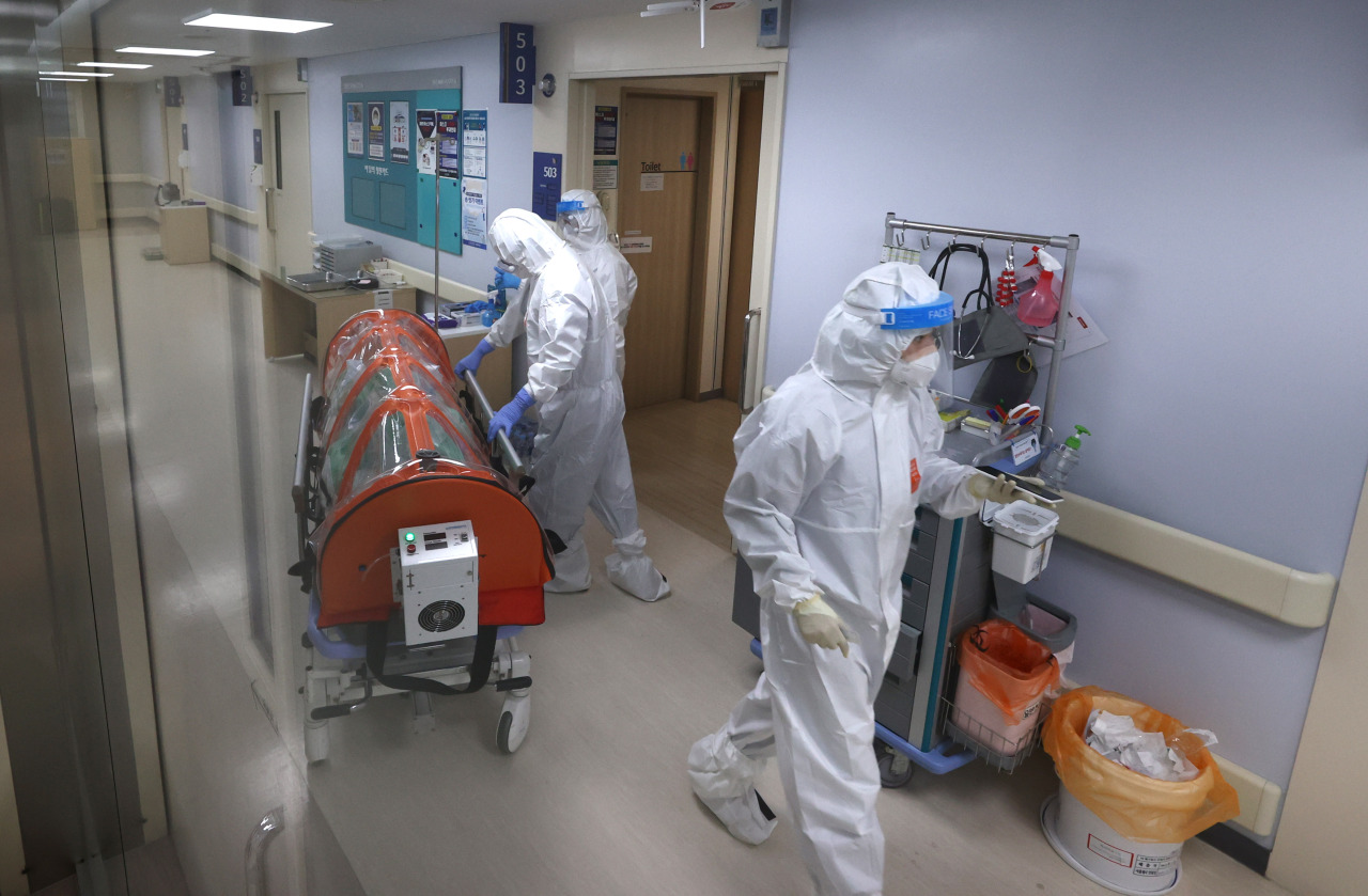 Health workers in protective suits help transfer a COVID-19 patient at a hospital in Seoul's eastern Gwangjin district on Tuesday. (Yonhap)