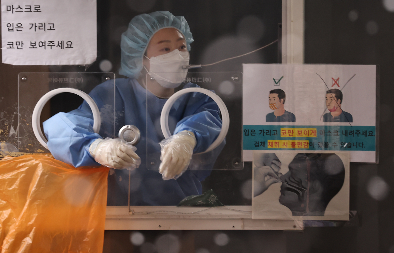 지난 19일 서울 중구 서울역 광장 코로나19 임시 선별검사소에서 눈이 내리는 가운데 의료진이 검사자를 부르고 있다. [연합]
