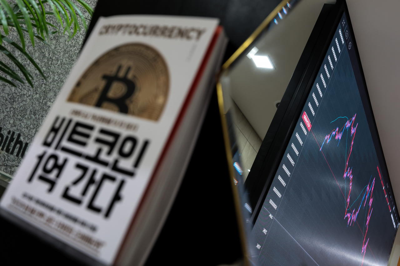 서울 빗썸 강남센터에 놓인 비트코인 관련 서적 뒤로 가상화폐 시세 그래프가 표시되고 있다.[연합]