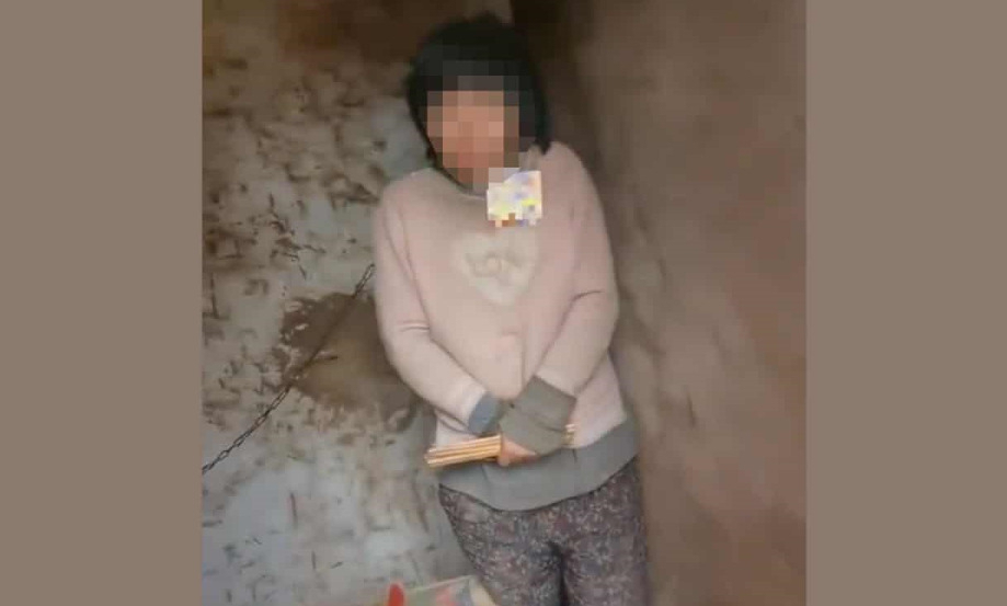 한 여성이 벽에 고정된 쇠사슬로 목이 묶인채 움추리고 서 있다. [가디언]
