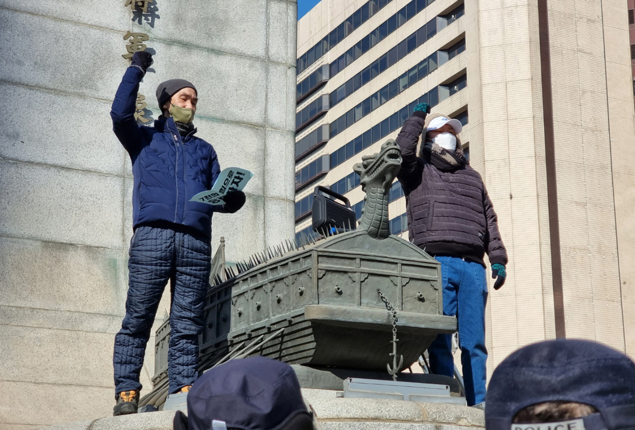 택배노조 조합원들이 지난달 22일 서울 종로구 광화문광장 이순신 동상에 올라가 CJ대한통운과 대화를 촉구하며 구호를 외치고 있다. [연합]