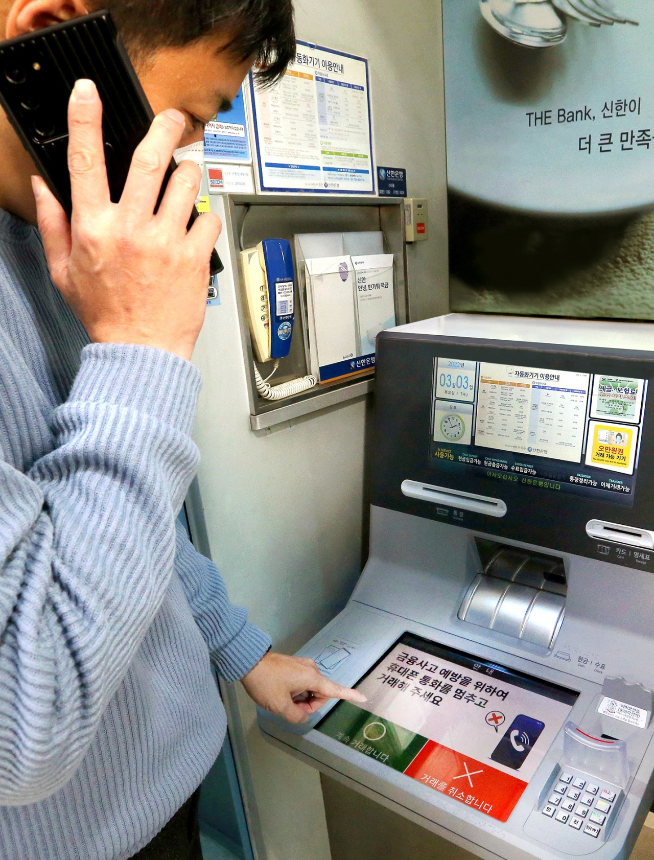 핸드폰 통화하며 신한은행 ‘AI 이상행동탐지 ATM’을 이용하고 있는 도중 ATM 화면에 금융사고 예방 주의 문구가 나오는 모습