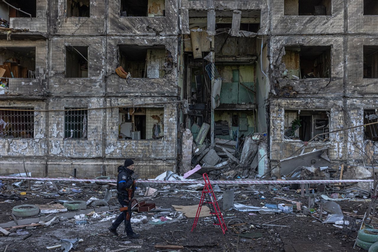 A Ukrainian police officer stands guard next to the residential building which was hit by the Russian artillery shelling, in the Obolon district, in Kyiv, Ukraine, Monday. At least two people reportedly have been killed after the artillery shelling. Russian troops entered Ukraine on Feb. 24, prompting the country's president to declare martial law and triggering a series of announcements by Western countries to impose severe economic sanctions on Russia. (EPA-Yonhap)