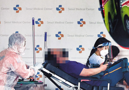 지난 3월 17일 코로나19 전담병원인 서울 중랑구 서울의료원에서 119 구급대원과 의료진이 병원에 도착한 환자를 감염병 전문 병동으로 이송하고 있다. [연합]