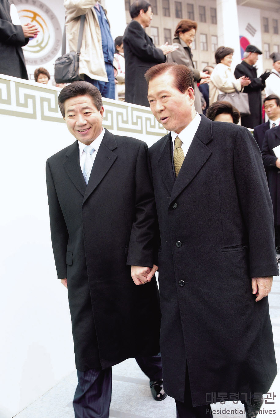 노무현 전 대통령이 2003년 2월 25일 여의도 국회의사당 광장에서 열린 제 16대 대통령 취임식에 참석한 뒤 전임인 김대중 전 대통령과 손을 맞잡고 걸어가고 있다. [대통령기록관]