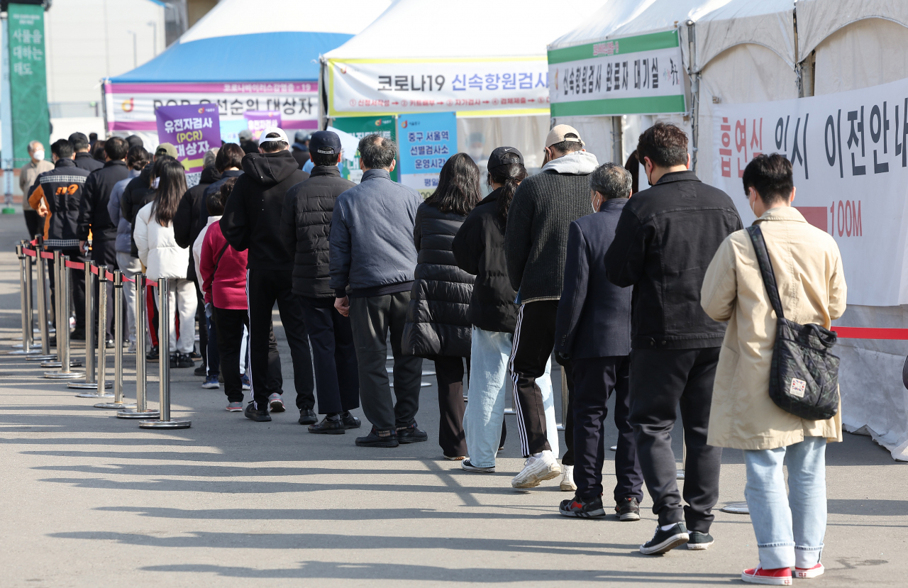 People stand in line to take coronavirus tests at a makeshift testing station in front of Seoul Station on Sunday. South Korea reported 318,130 new virus cases on the day. (Yonhap)