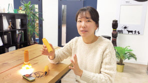 장성은 요크 대표가 태양광으로 충전할 수 있는 랜턴 ‘솔라밀크’를 들고 설명하고 있다. 아이들은 솔라밀크를 들고 학교에 나와, 학교에 비치된 소 모양의 태양광 발전기(윗사진)로 전력을 얻어 가정으로 가져간다. [요크 유튜브 캡처]
