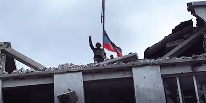 한 러시아 병사가 28일(현지시간) 우크라이나 남동부 항구도시 마리우폴 시청 건물 꼭대기에 올라가 도네츠크인민공화국(DPR·노란색 원내) 국기를 게양한 뒤 손을 들어 올리며 환호하고 있다. [The Telegraph 유튜브 캡처]