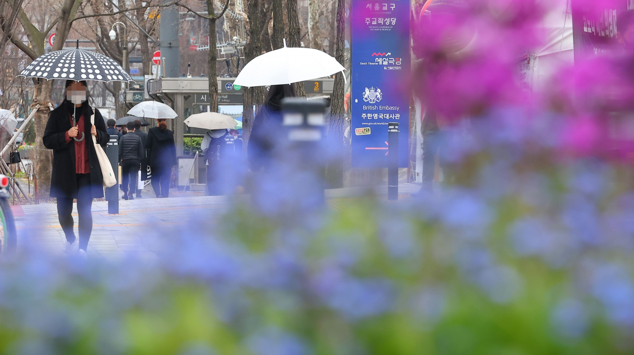 지난달 30일 오후 비가 내린 서울 종로구 세종대로의 한 화단 뒤로 우산을 쓴 시민이 길을 지나고 있다. [연합]