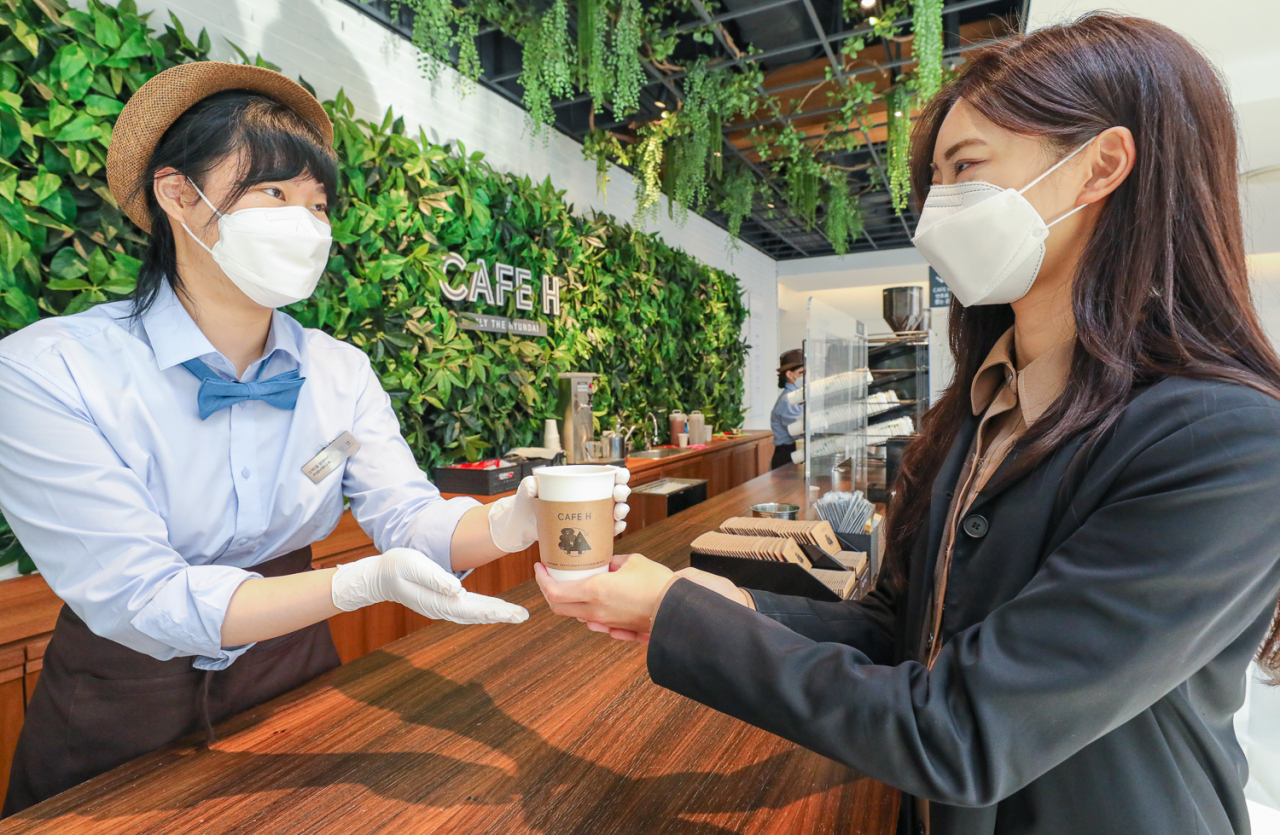 현대백화점이 100% 재활용이 가능한 ‘친환경 종이컵’을 도입한다. 무역센터점 11층 카페H 직원이 친환경 종이컵을 고객에게 전달하는 모습.[현대백화점 제공]