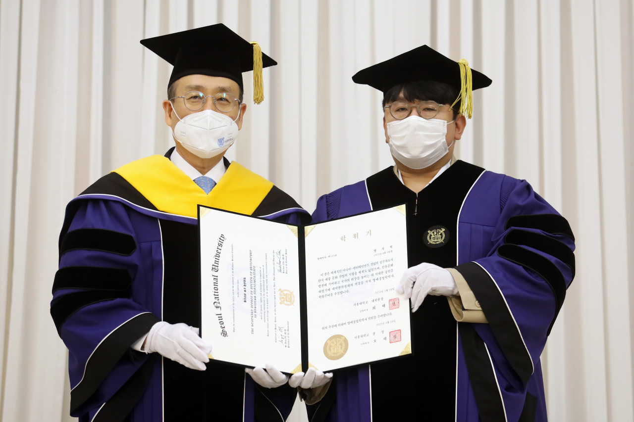Seoul National University President Oh Se-jung (left), and Hybe Chairman Bang Si-hyuk pose for picture during the awarding ceremony of Bang’s honorary doctorate degree from the university that took place in SNU Seoul campus on Thursday. (Yonhap)