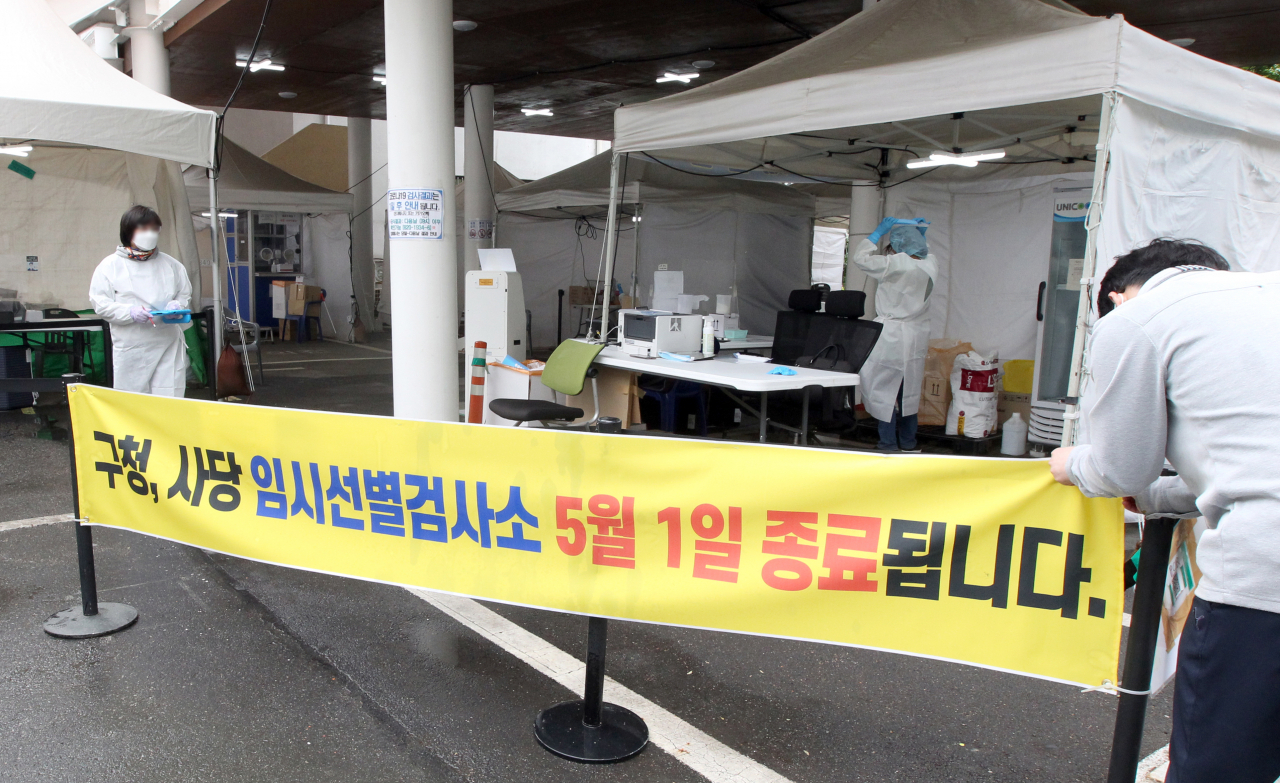 서울 동작구청 관계자가 29일 동작구청과 사당문화회관에 설치된 코로나19 임시선별검사소가 오는 5월 1일부터 종료된다는 안내문을 부착하고 있다. [연합]