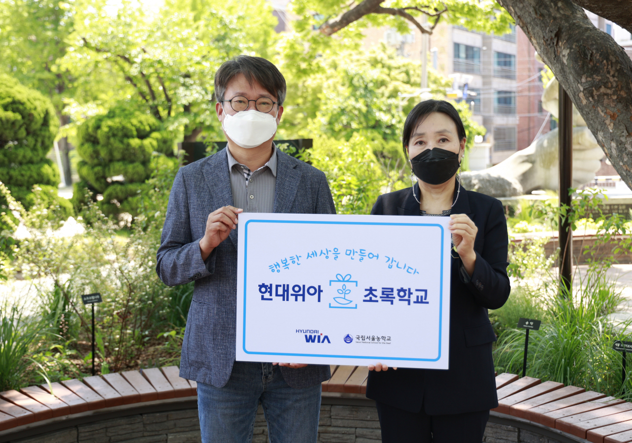 현대위아 원광민 차량부품연구센터장(왼쪽)과 국립서울농학교 김은숙 교장이 지난 10일 서울 종로구 국립서울농학교 내 현대위아가 조성한 ‘느티나무 정원’에서 기념사진을 찍고 있다. [현대위아 제공]