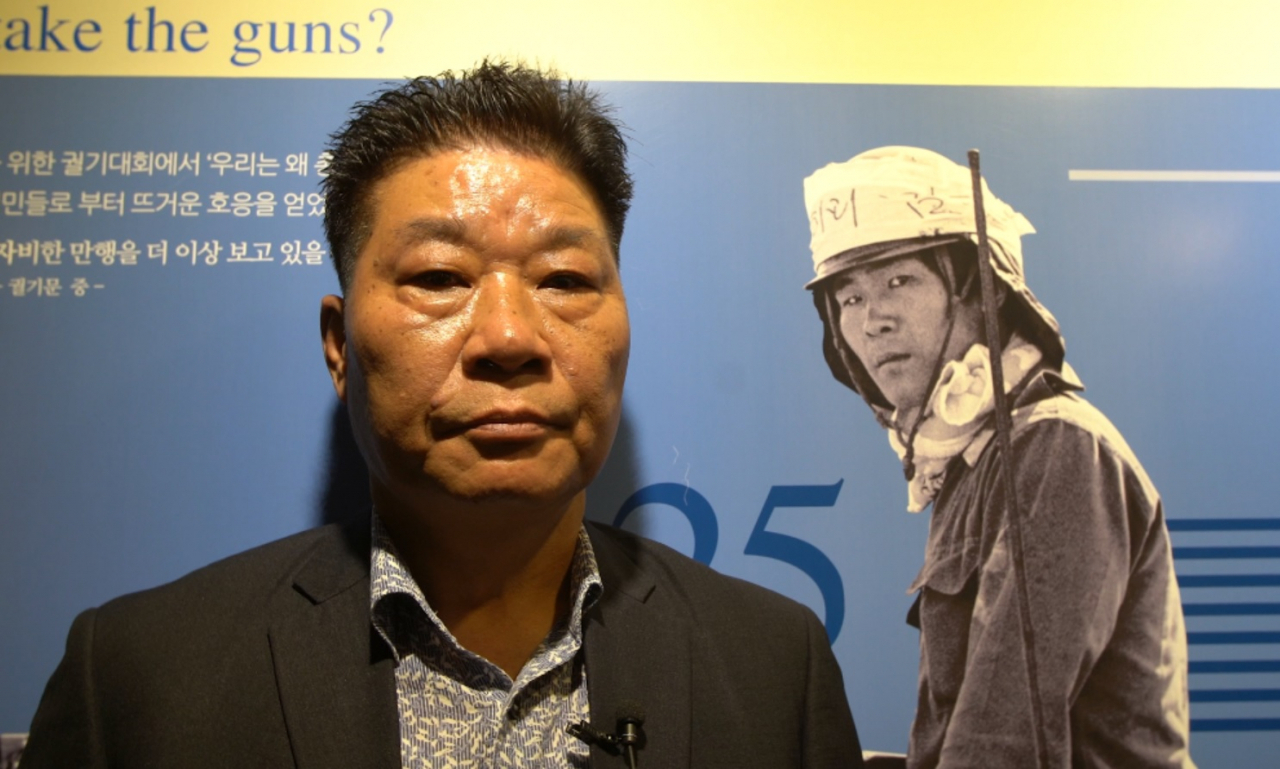 5·18 민주화운동진상규명조사위원회는 12일 대국민보고회에서 다큐멘터리 영화 '김군'의 사진 속 시민군이 살아 있다고 밝혔다. 북한군 광수 1번으로 지목됐던 차복환 씨가 논란의 사진을 배경으로 촬영하고 있다. [5·18진상규명위 제공]