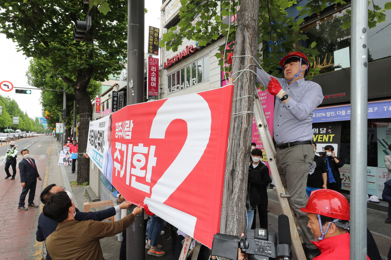국민의힘 이준석 대표가 20일 오전 광주 북구 전남대학교 후문 앞 거리에서 전날 고의 훼손된 광주 후보자들의 현수막을 다시 달아주고 있다. [연합]
