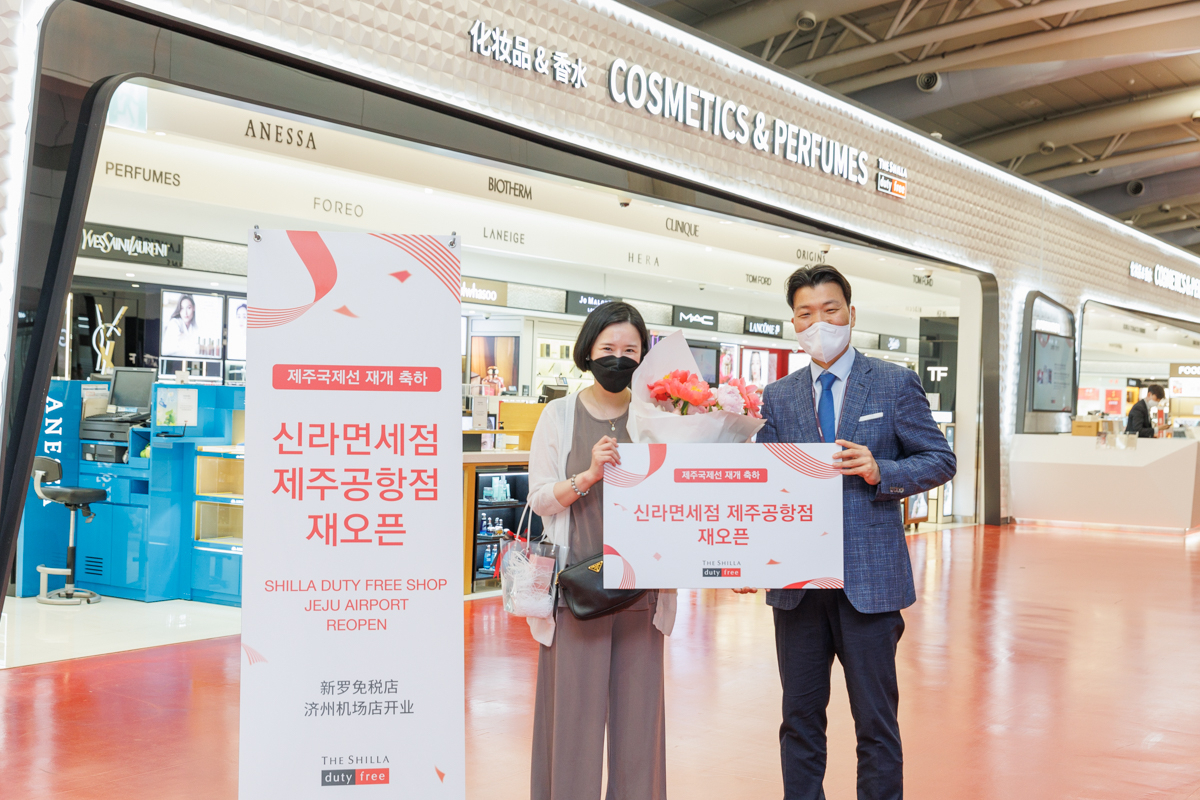 지난 2일 신라면세점 제주국제공항점이 재오픈했다. 윤재필 신라면세점 제주공항점장(사진 오른쪽)이 재오픈 첫 구매 고객에게 꽃다발과 함께 기념품을 선물로 증정하고 기념촬영을 하고 있다.[신라면세점 제공]