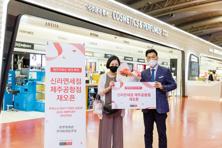 윤재필(오른쪽) 신라면세점 제주공항점장이 재오픈 첫 구매 고객에게 꽃다발과 함께 기념품을 선물로 증정하고 기념촬영을 하고 있다. [신라면세점 제공]