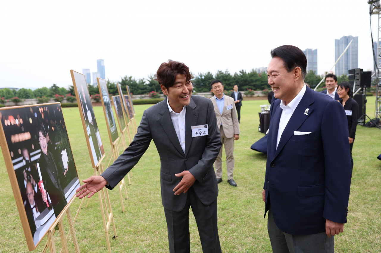 윤석열 대통령이 12일 오후 서울 용산 대통령실 청사 잔디마당에서 열린 영화관계자 초청 만찬에서 한국 배우 최초로 칸국제영화제에서 남우주연상을 수상한 배우 송강호와 사진을 보며 대화하고 있다. [연합]