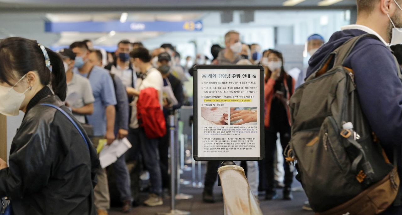 Foreign entrants are waiting for quarantine at the arrival hall of Terminal 1 of Incheon International Airport on May 24. In front of the passengers, a notice about monkey pox is erected. (Yonhap)