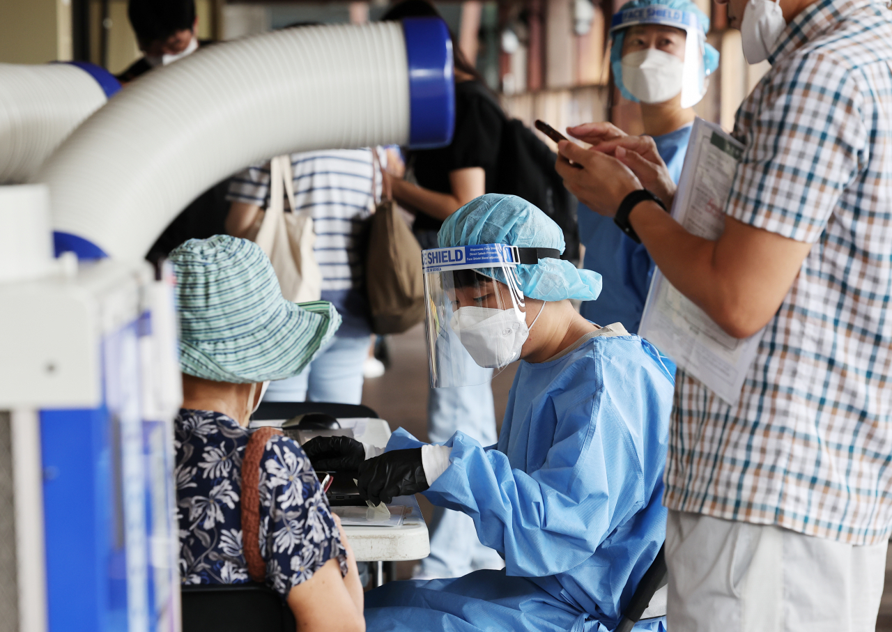 A health worker talks to a visitor before conducting a COVID-19 PCR test at a testing station in Seoul's eastern district of Songpa on Thursday. (Yonhap)