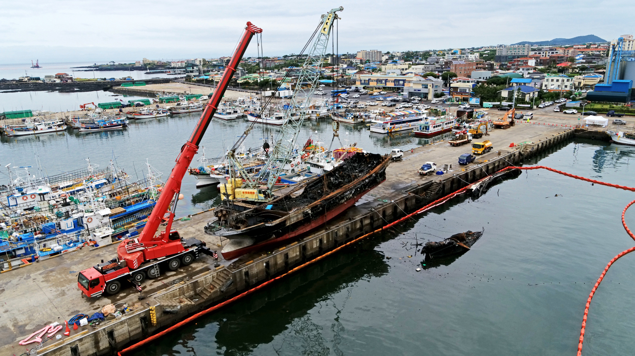 Two cranes carry out an operation to lift a burnt fishing boat at Hallim Port on Jeju Island on Monday. (Yonhap)