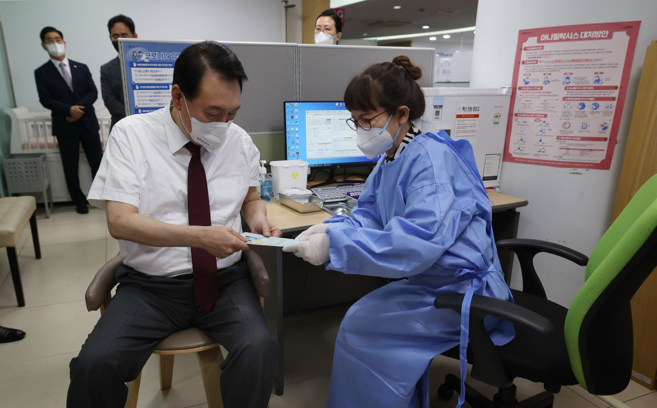 President Yoon Suk-yeol (left) speaks with a health care worker before receiving his fourth dose of the Pfizer vaccine on Wednesday at a public health clinic in Jung-gu, a central Seoul district. (Yonhap)