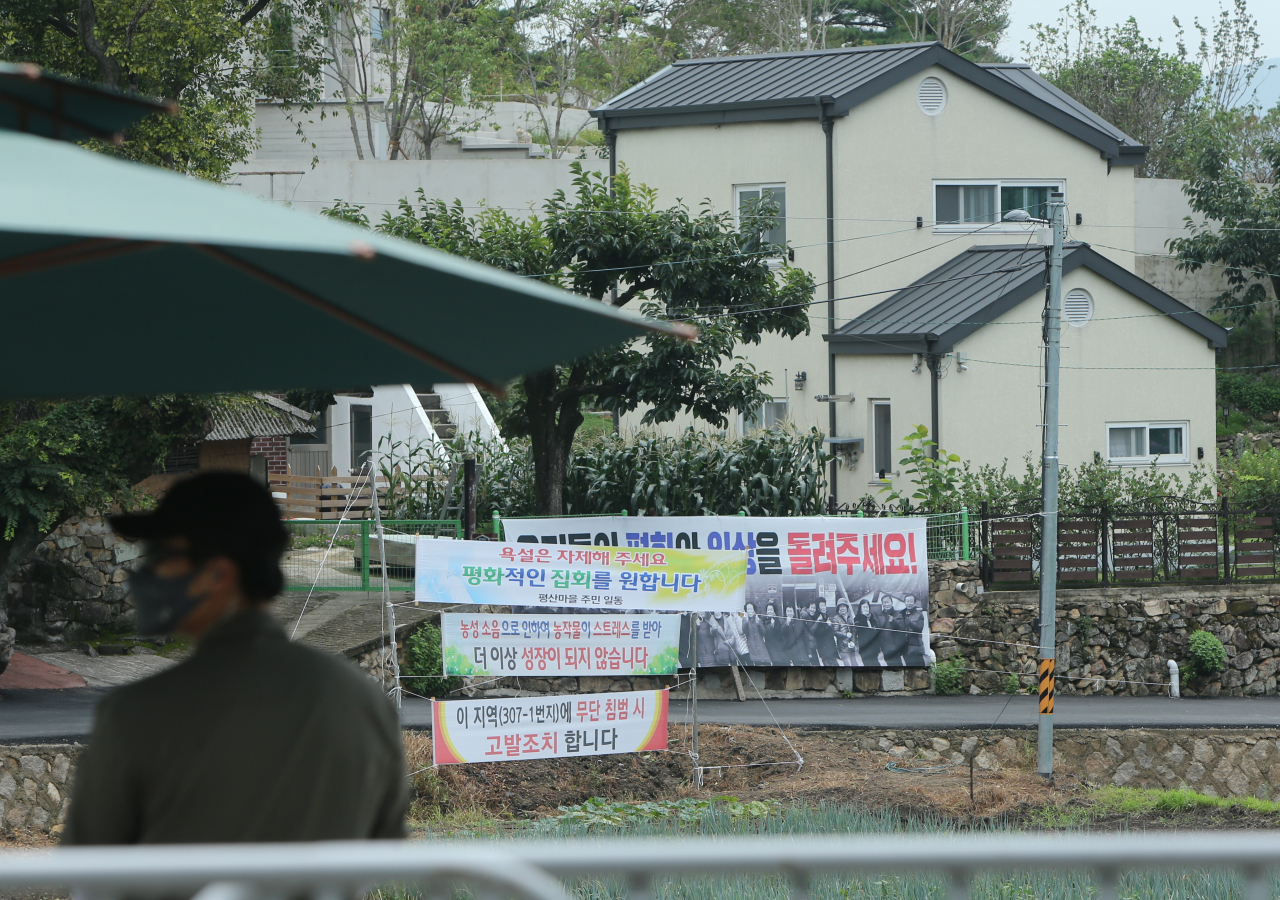 14일 낮 경남 양산시 하북면 지산리 평산마을 문재인 전 대통령 사저(오른쪽 건물 뒤쪽 일부분만 보이는 건물) 앞에 '우리들의 평화와 일상을 돌려주세요' '욕설은 자제해주세요. 평화적인 집회를 원합니다' 등이 적힌 현수막이 걸려 있는 가운데 경호처 직원이 사저 경비를 서고 있다. [연합]
