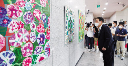 윤석열 대통령이 25일 오전 서울 용산 대통령실 청사로 출근하며 희망, 도약, 통합 메시지를 담은 발달장애 아티스트들의 작품을 살펴보고 있다. [연합]
