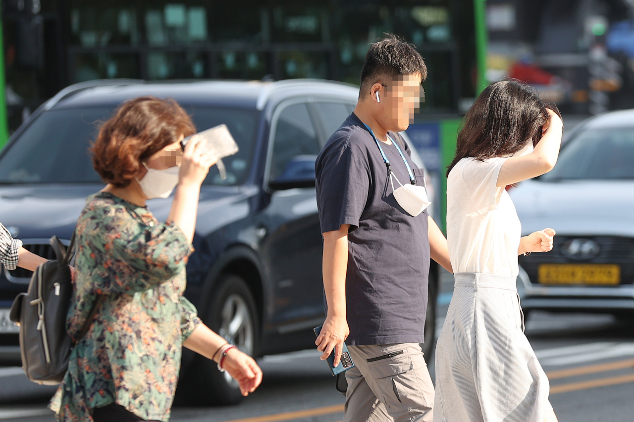 지난 26일 오전 서울 광화문 네거리에서 시민들이 손과 스마트폰으로 햇빛을 가린 채 횡단보도를 건너고 있다. [연합]