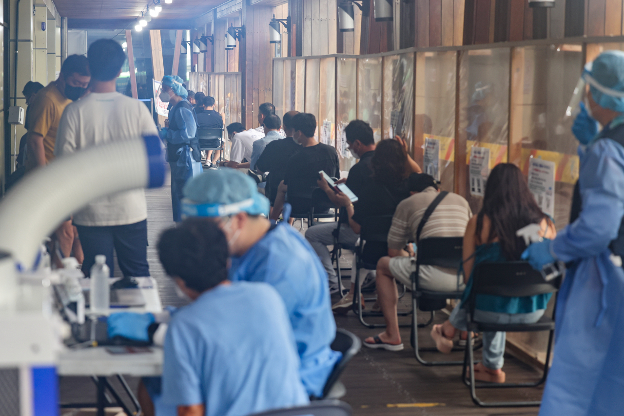 People sit in line to receive tests at a COVID-19 testing center in Seoul last Tuesday. (Yonhap)