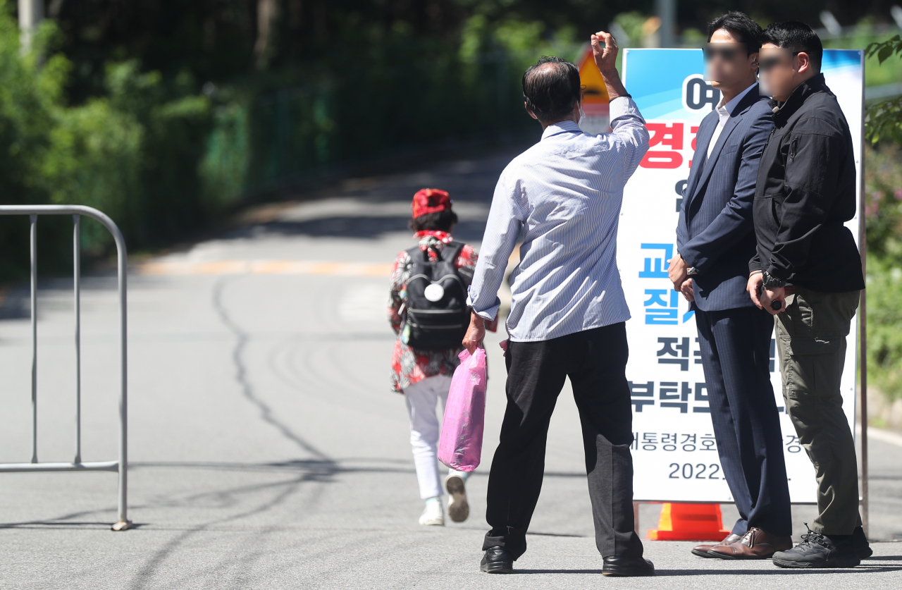 문재인 전 대통령 내외 사저 경호 강화 첫날인 22일 오전 사저에서 300여ｍ 떨어진 경남 양산시 하북면 평산마을 입구에서 경호처 직원이 방문객에게 방문 목적 등을 묻고 있다. 한 시민이 유튜브 방송을 위해 현장을 찾았다고 방문 목적을 밝히는 모습. 이날부터 문 전 대통령 내외 사저 300ｍ 떨어진 곳에서 대통령 경호처, 경찰이 위험물질 등을 검문 검색한다. [연합]