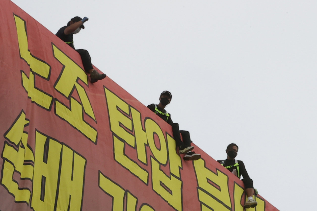 지난 18일 서울 강남구 하이트진로 본사에서 고공농성을 펼치고 있는 화물노동자들이 화물연대 고공농성투쟁 승리 결의대회 참가자들의 격려에 호응하고 있다. [연합]