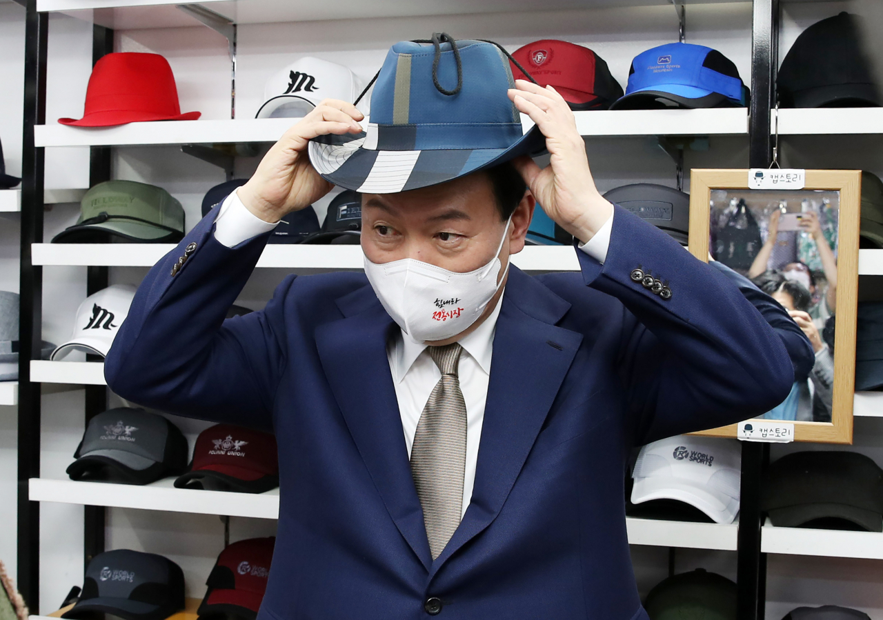 윤석열 대통령이 26일 오후 대구 중구 서문시장 내 모자 가게를 방문, 모자를 써보며 상인들과 대화하고 있다. [연합]