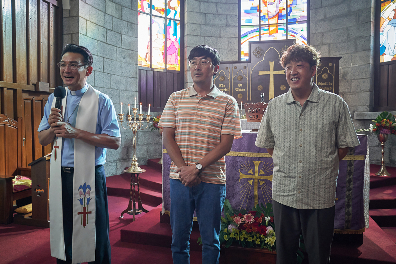A still image shows Hwang Jung-min (left) as Pastor Jeon and Ha Jung-woo (center) as Kang In-gu at a church in "Narco-Saints." (Netflix)
