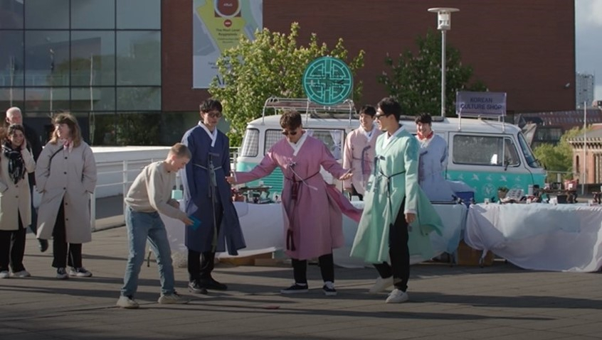 A still image shows the cast of "Dopojarak: Story of Homme the K-Wanderer" playing a traditional Korean game with people in Denmark. (MBC)