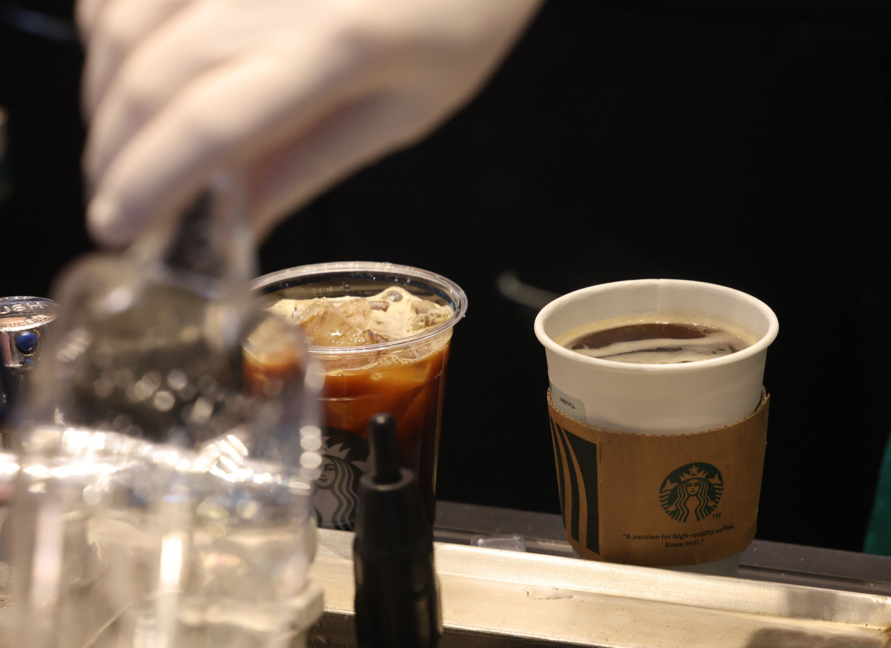 An employee prepares coffee in single-use cups at a cafe in Seoul on Sept. 13. (Yonhap)