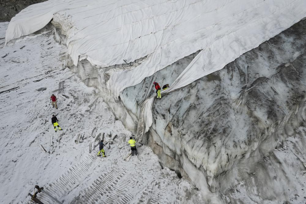 People work on a tarpaulin which cover the ice of the Corvatsch glacier, near Samedan, Switzerland, on Sept. 5, Glaciologists have stopped their program to measure the glacier. The decision has already been taken in 2019 and the hot summer of 2022 has led to "extreme losses of ice" and the end of the program. The covered part of the glacier is used as a ski slope in winter. (Gian Ehrenzeller/Keystone via AP,file)