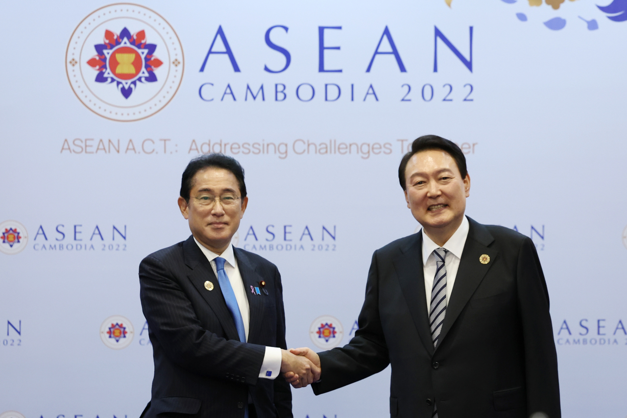 President Yoon Suk-yeol shakes hands with Japanese Prime Minister Fumio Kishida and takes a commemorative photo at the Korea-Japan summit held at a hotel in Phnom Penh, Cambodia on Sunday. (Yonhap)