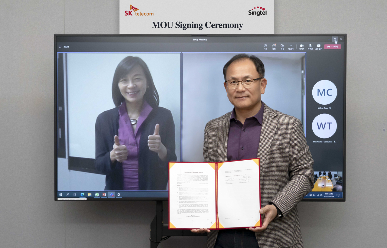 Ha Min-yong (right), chief development officer of SK Telecom, poses for a photo with Anna Yip (on screen), Singtel’s chief executive officer of consumer, after a signing ceremony held by video conference on Monday. (SK Telecom)