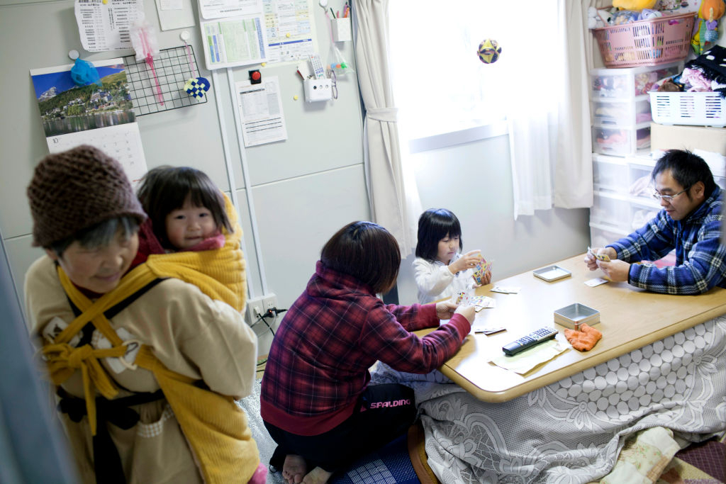 2011년 동일본 대지진 때 북부 이와테 현 리쿠젠타카타 시에 거주하는 지진 생존자 가족들의 2011년 12월 4일 모습이다. 7세 첫째는 부모와 카드놀이를 하고 있고, 할머니는 둘째를 포대기로 업고 있다. [게티이미지]