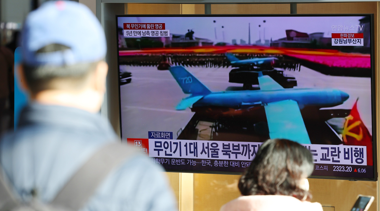 Passersby watch a news report on North Korean drones' infiltration into South Korean airspace at Yongsan Station in Seoul on Tuesday. (Yonhap)