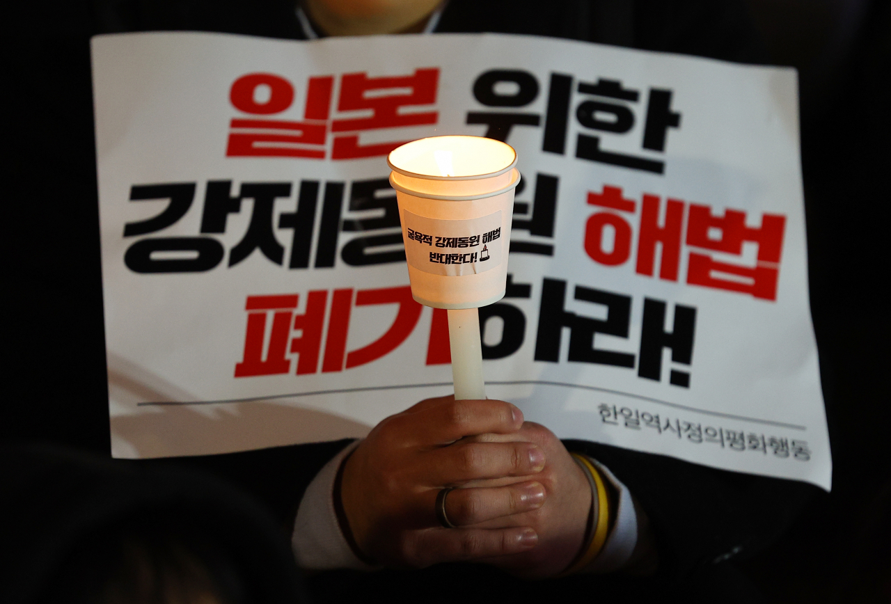 13일 오후 서울 중구 서울파이낸스빌딩 앞에서 열린 윤석열 정부의 강제동원 해법 발표 규탄 집회에서 참가자가 촛불과 피켓을 들고 있다. [연합]