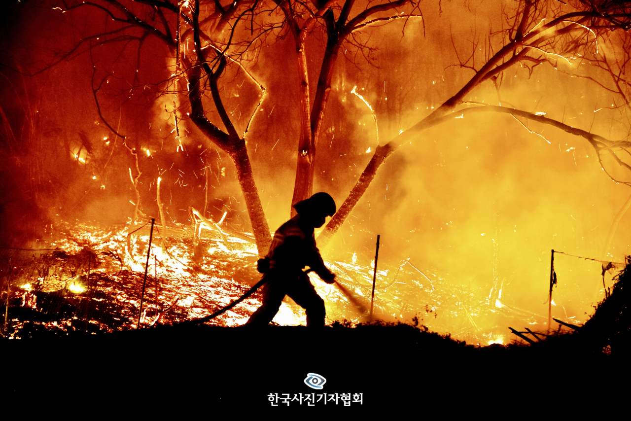 〈최우수상 - 산불과 소방관의 뜨거운 사투〉 울진 산불이 발생한 가운데 경북 울진군 북면 고목1리에서 소방관이 야간 진화 작업을 하고 있다. 이날 발생한 산불은 한국 역사상 가장 긴 213시간 동안 이어졌다. 〈이현덕 기자 / 영남일보 / 한국사진기자협회〉